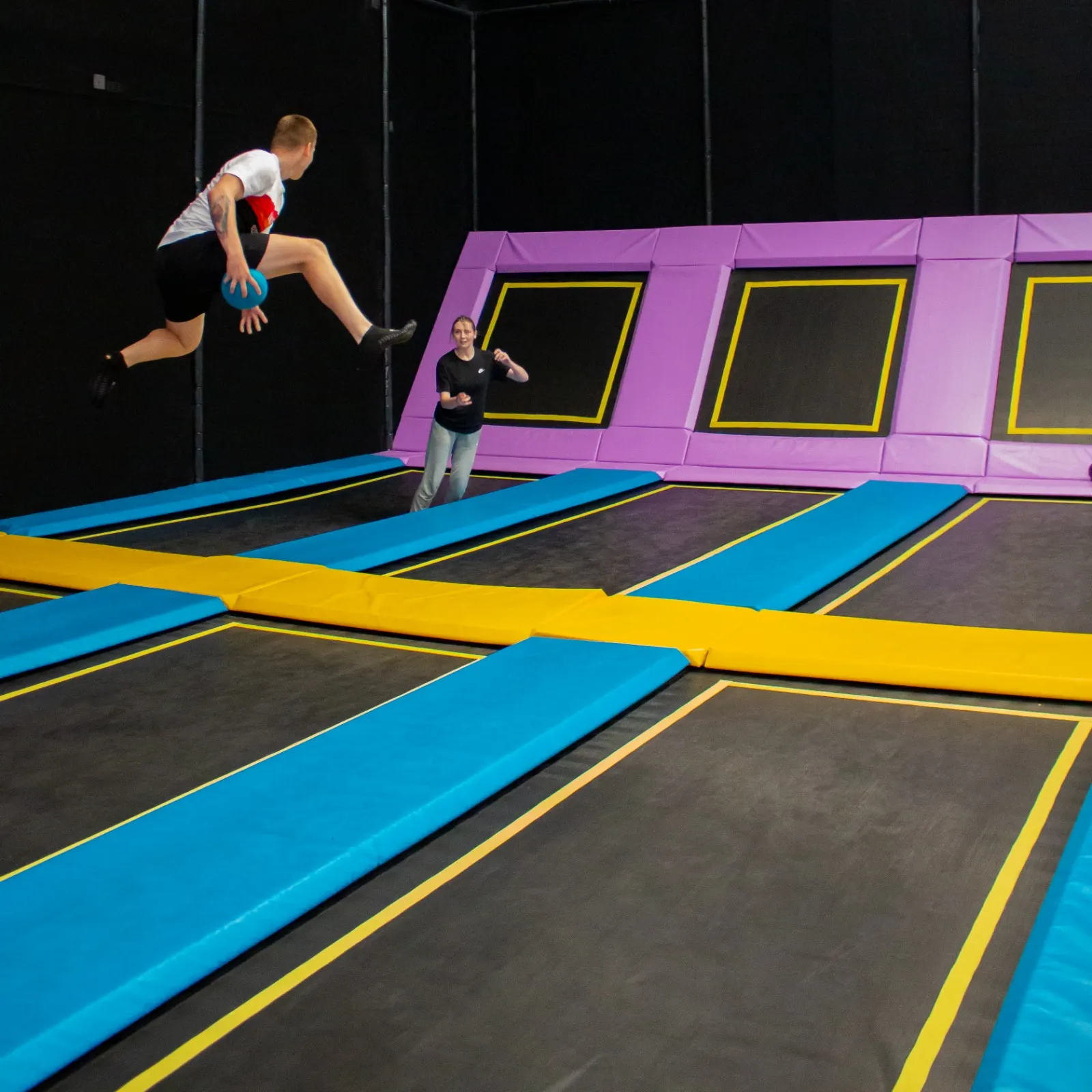 Un enfant en plein saut au-dessus des trampolines, avec un adulte à proximité